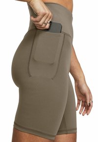 Une main glissant un smartphone dans la poche latérale d'un short de sport ajusté taille haute de couleur taupe.