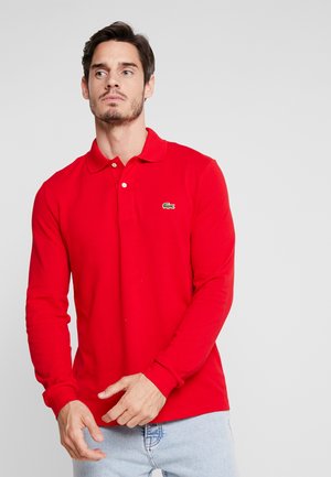 Röd långärmad polo skjorta med en tre-knapp placket, ribbade muddar och en liten grön krokodil-logotyp på vänster bröst. Slät tygkvalitet.