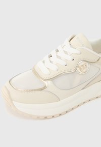 Αθλητικό παπούτσι κρεμ χρώματος με πάνελ από δίχτυ, μεταλλικές λεπτομέρειες και λευκά κορδόνια. Διαθέτει διακριτικό λογότυπο και υφασμένο πέλμα για καλύτερη πρόσφυση.