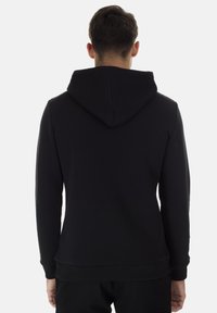 Sudadera con capucha negra, fabricada en un tejido suave, que presenta un ajuste relajado, puños y cintura acanalados, con una textura lisa y sin logotipos visibles.