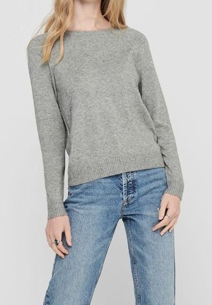 Maglione grigio lavorato a maglia con scollatura ampia, maniche lunghe e orlo a costine, abbinato a jeans chiari a vita alta. Texture liscia.