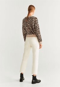 Suéter de punto con estampado de leopardo sobre una base beige, combinado con jeans rectos de color claro y botas de tobillo negras. La silueta es relajada.