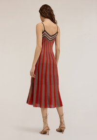 Robe tricot rayée rouge et grise avec un corsage ajusté et une jupe évasée, dotée de fines bretelles et d'un motif en chevron dans le dos.