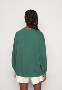 Vihreä, ylisuurikokoinen collegepaita puuvillasekoitetta, jossa pyöreä pääntie ja lasketut olkapäät, yhdistettynä valkoisiin, rispaantuneilla reunoilla varustettuihin shortseihin.