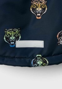 Mörkt tyg med ett livligt tigermönster i olika färger. Inkluderar en rektangulär, slät etikett med präglad text.