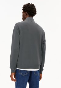 Sudadera gris con un cuello alto, puños y dobladillo acanalados. La tela parece suave, combinada con unos jeans azules texturizados y una camiseta blanca debajo.