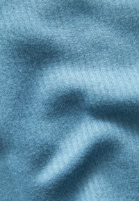 Lichtblauwe gebreide stof, met een zachte textuur en een gladde afwerking. Het materiaal toont subtiele variaties in kleur en weefpatroon.