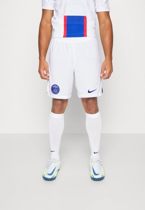 Mand iført hvide Paris Saint-Germain fodboldshorts, hvide sokker og hvide Nike fodboldstøvler står mod en ensfarvet baggrund.