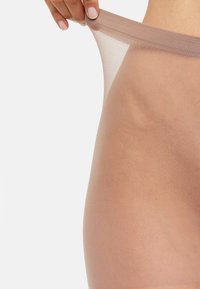 Collant trasparenti color pelle che vengono tirati, dotati di una texture morbida e di una vita elastica. Aspetto liscio con dettagli di design minimi.