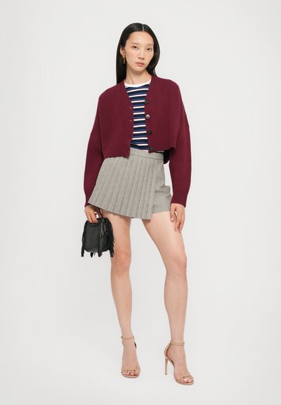 Burgundy lyhi kardigan dengan penutup kancing, atasan bergaris navy dan putih, rok mini pleats abu-abu, dan tas tangan fringing hitam.