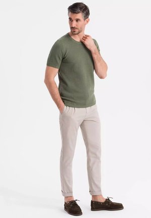 Olivově zelený svetr s krátkým rukávem s texturovaným povrchem, kombinovaný se světlými béžovými kalhotami slim fit a tmavě hnědými volnočasovými botami.