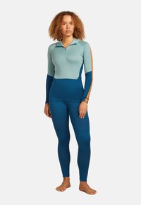 Långärmad zip-up topp i ljusblått och mörkblått med orange detaljer; ihop med mörkblå leggings; tyget verkar slätt och elastiskt.
