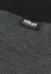Tejido a rayas negro y gris con una banda negra en la cintura y una etiqueta negra que dice "IUMAN intimissimi uomo" cosida cerca del borde superior.