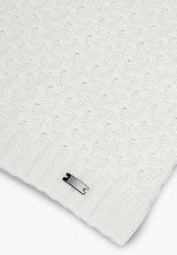 Pull blanc tricoté avec un motif texturé, doté de poignets côtelés et d'une petite étiquette de marque métallique à l'ourlet. Matière douce, semblable à de la laine.