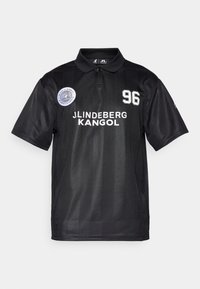 Sort polo skjorte med krave, prydet med hvid tekst "J. Lindeberg Kangol" og nummeret "96", samt et rundt logo på venstre side.