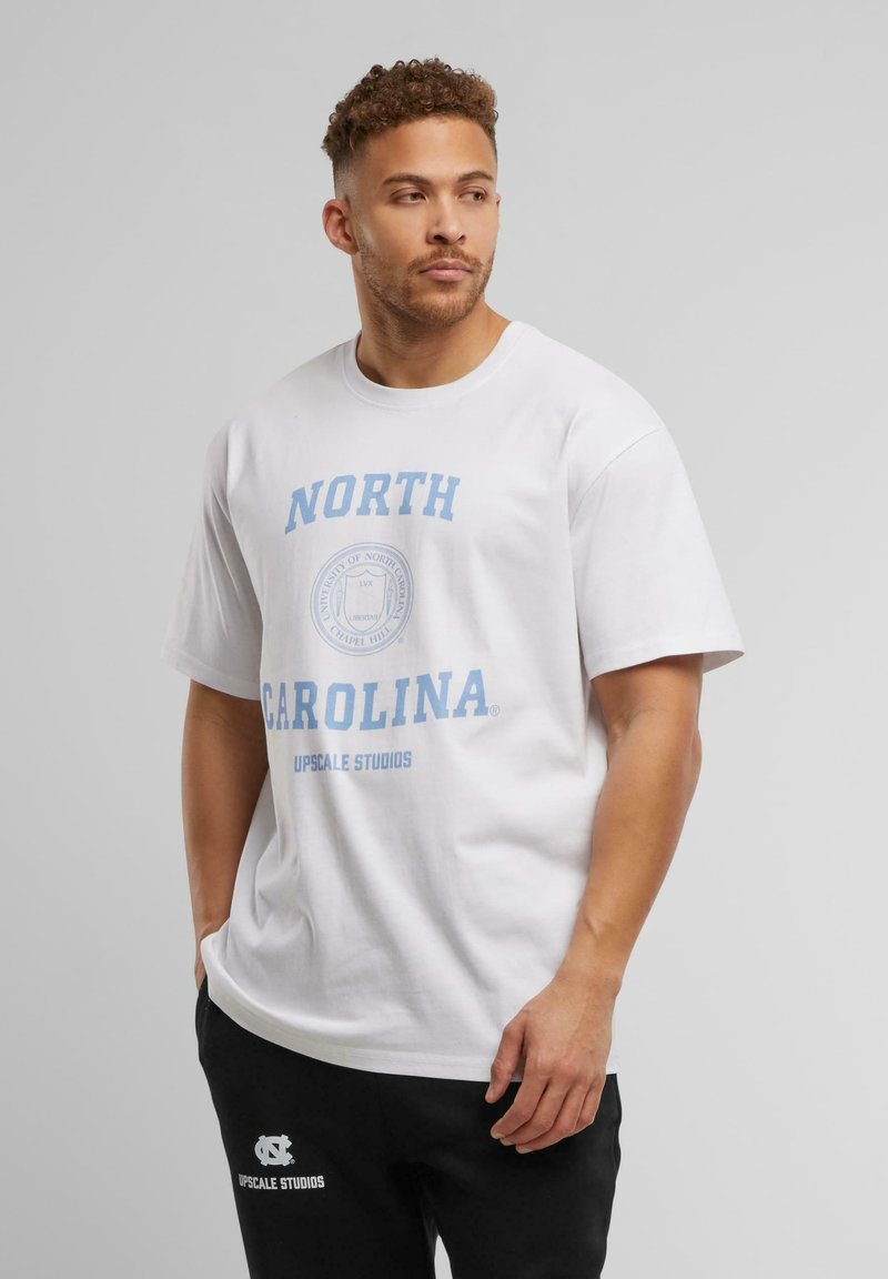 Hvid bomuld t-shirt med blå tekst "NORTH CAROLINA" og et rundt emblem samt "UPSCALE STUDIOS." Løs pasform med korte ærmer.
