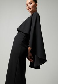 Musta, pitkän mitaltaan oleva mekko, jossa on dramaattinen viittakuvio, istuva vartalonmyötäinen yläosa ja sileä pinta. Elegantti tyyli, jossa on minimalisia muotoiluelementtejä.