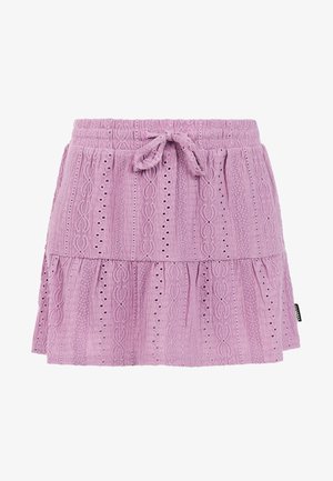 Grünes Tanktop mit pinken Buchstaben kombiniert mit einem mehrstufigen, hellvioletten Rock mit Lochstickereien. Model trägt leichte Sandalen.