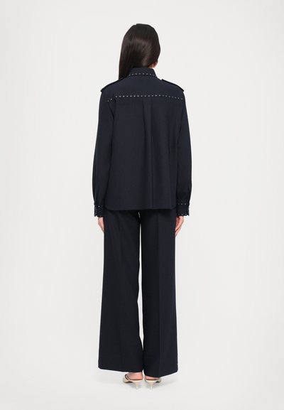 Navy blue two-piece outfit featuring a long-sleeve shirt with studs on the shoulders and cuffs, paired with wide-leg trousers.