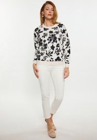 Blumenmuster-Pullover in Schwarz und Weiß, runder Halsausschnitt, lange Ärmel, kombiniert mit weißen Slim-Fit-Hosen und beigen Schuhen.