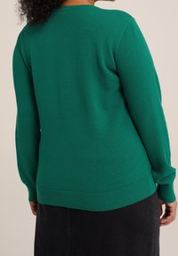 Grön texturerad tröja med rund halsringning, ribbade muddar och nederkant. Materialet har ett mönster som liknar små diamanter.