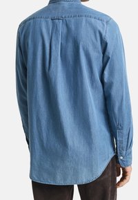 Lichtblauw denim overhemd met een button-down kraag, lange mouwen en een afgeronde zoom. Voorzien van een plooitje in het midden van de rug en manchetknopen.
