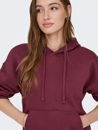 Sweat à capuche bordeaux avec une poche avant, un cordon de serrage et une coupe ample. Matière en coton doux et texture côtelée aux poignets et à l'ourlet.