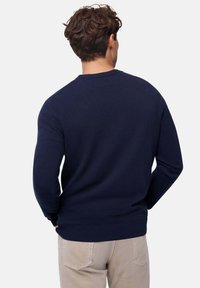 Pull navy a girocollo realizzato in tessuto morbido con maniche lunghe e orlo a coste, indossato con pantaloni beige chiaro, visto da dietro.