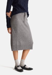 Šedá pletená sukně s žebrovaným lemem a páskem na stažení, doplněná černými Mary Jane botami a světle šedými kotníkovými ponožkami.