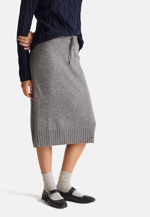 Jupe en tricot gris avec un ourlet côtelé et une taille à cordon, associée à des chaussures Mary Jane noires et des chaussettes mi-mollet grises claires.