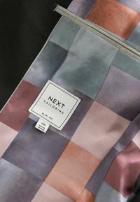 Veste ajustée avec une doublure à carreaux multicolore dans des tons pastel de rose, violet et bleu-vert, avec une étiquette en tissu "NEXT TAILORING."