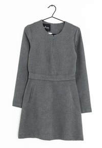 Robe en tricot grise avec des manches longues, un col rond et une taille cintrée. Elle présente deux poches latérales et une fermeture éclair au dos.