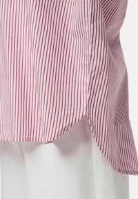 Camicia a righe rosa e bianche con spacco laterale, realizzata in tessuto leggero con una texture liscia. Il motivo è uniforme in tutto il capo.