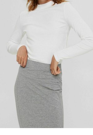 Woman wearing white long-sleeve top adjusting the waistband of a fitted grey skirt against a plain background.