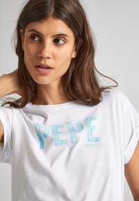 Balta kokvilnas T-kreklu ar gaiši zilu "PEPE JEANS" logo. Apaļa kakla izgriezums, īsās piedurknes un brīvs piegriezums. Gluda tekstūra.