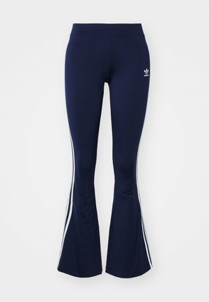 Leggings évasés bleu marine en tissu extensible, dotés de rayures blanches sur les côtés et d'un petit logo à l'avant. Texture lisse sur l'ensemble.