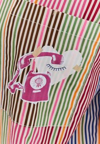 Material w paski w kolorach takich jak zieleń, róż, brąz i pomarańcz. Zawiera grafikę różowego telefonu na sercu, wzmocnioną taśmą.