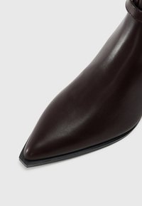 Botte en cuir marron à cheville avec un bout pointu, texture lisse et semelle en caoutchouc noire. Présente un design minimaliste et sans matériel visible.