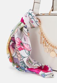 Borsa bianca con una sciarpa di raso floreale legata al manico, con dettagli in catena dorata e un charm a forma di farfalla.