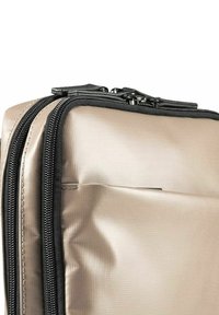 Borsa da viaggio beige con una texture lucida, doppie cerniere e dettagli neri. Presenta una forma rettangolare e una superficie liscia, leggermente imbottita.