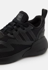 Svart sportskor med mesh-ovandel och syntetiska detaljer. Har tre ränder, snören och tjockt gummisula.