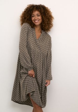 Vestito marrone a pois con maniche lunghe e scollo a V. Presenta una vita arricciata e un tessuto morbido e strutturato. L'orlo si ferma sopra il ginocchio.