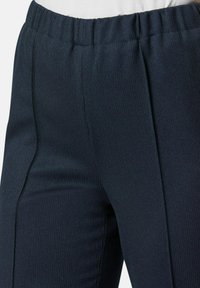 Marineblauwe ribbroeken met een elastische tailleband en verticale naden, die zorgen voor een gestructureerd oppervlak en een aansluitende pasvorm.