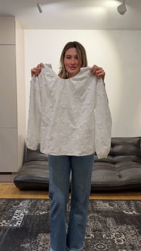 Moteris laiko baltą ilgomis rankovėmis palaidinę su gėlių siuvinėjimu moderniame svetainėje su juoda sofa.