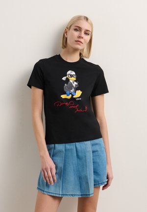 Black cotton t-shirt featuring a colorful Donald Duck graphic with glasses and a red signature, paired with a light blue pleated denim skirt.