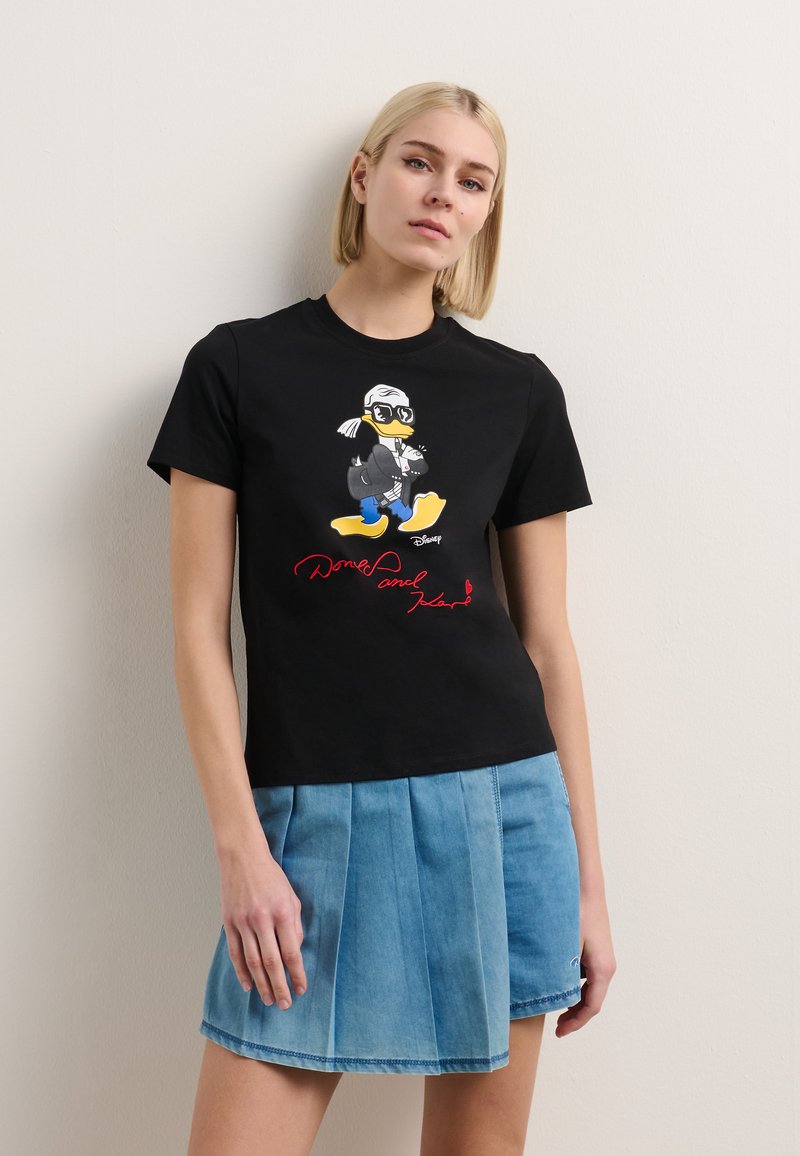 T-shirt noir en coton avec un graphique coloré de Donald Duck portant des lunettes et une signature rouge, associé à une jupe en denim plissée bleu clair.