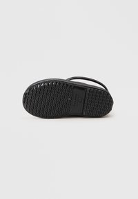 Semelle de sandale en caoutchouc noir avec un motif texturé et ondulé pour plus d'adhérence. Le design comprend des brides fines et un profil plat pour un look décontracté.