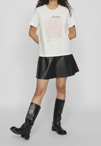 Camiseta blanca de manga corta con estampado floral rosa y texto, combinada con una falda negra de cuero sintético y botas negras hasta la rodilla.