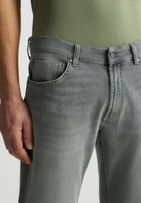 Jean gris de mezclilla con corte ajustado, que presenta un diseño de cinco bolsillos, passadores para cinturón y una sutil textura desgastada. Vista en primer plano que muestra la cintura delantera.