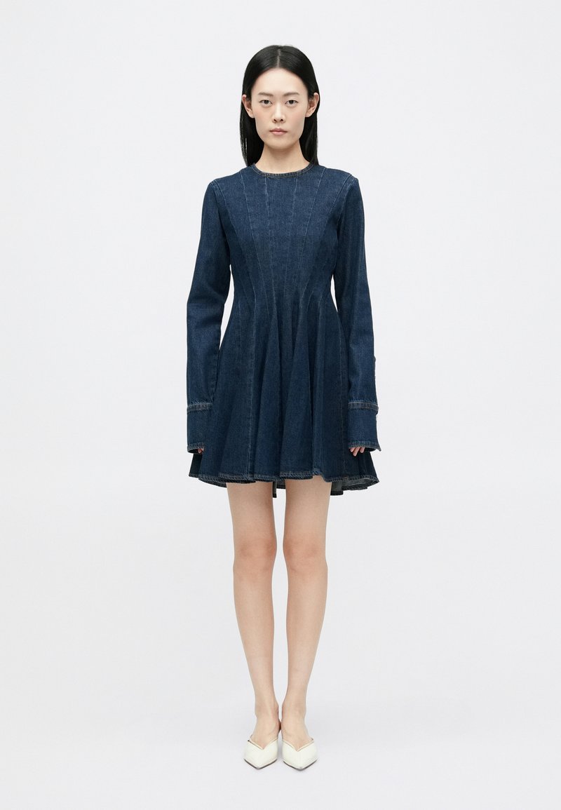 Robe en denim à manches longues, corsage ajusté et jupe évasée. Couleur bleu foncé, couture visible et encolure ronde.